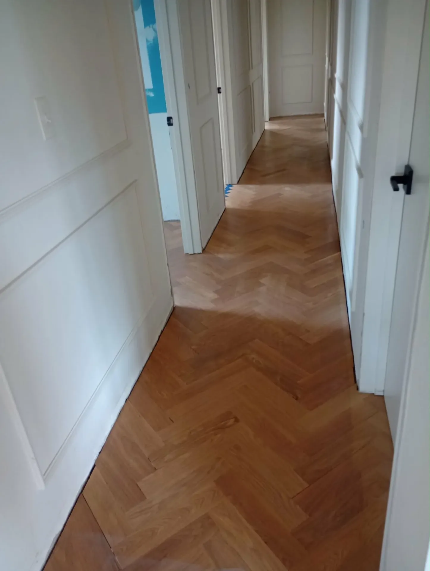 New herringbone hardwood floor running down a white paneled hallway