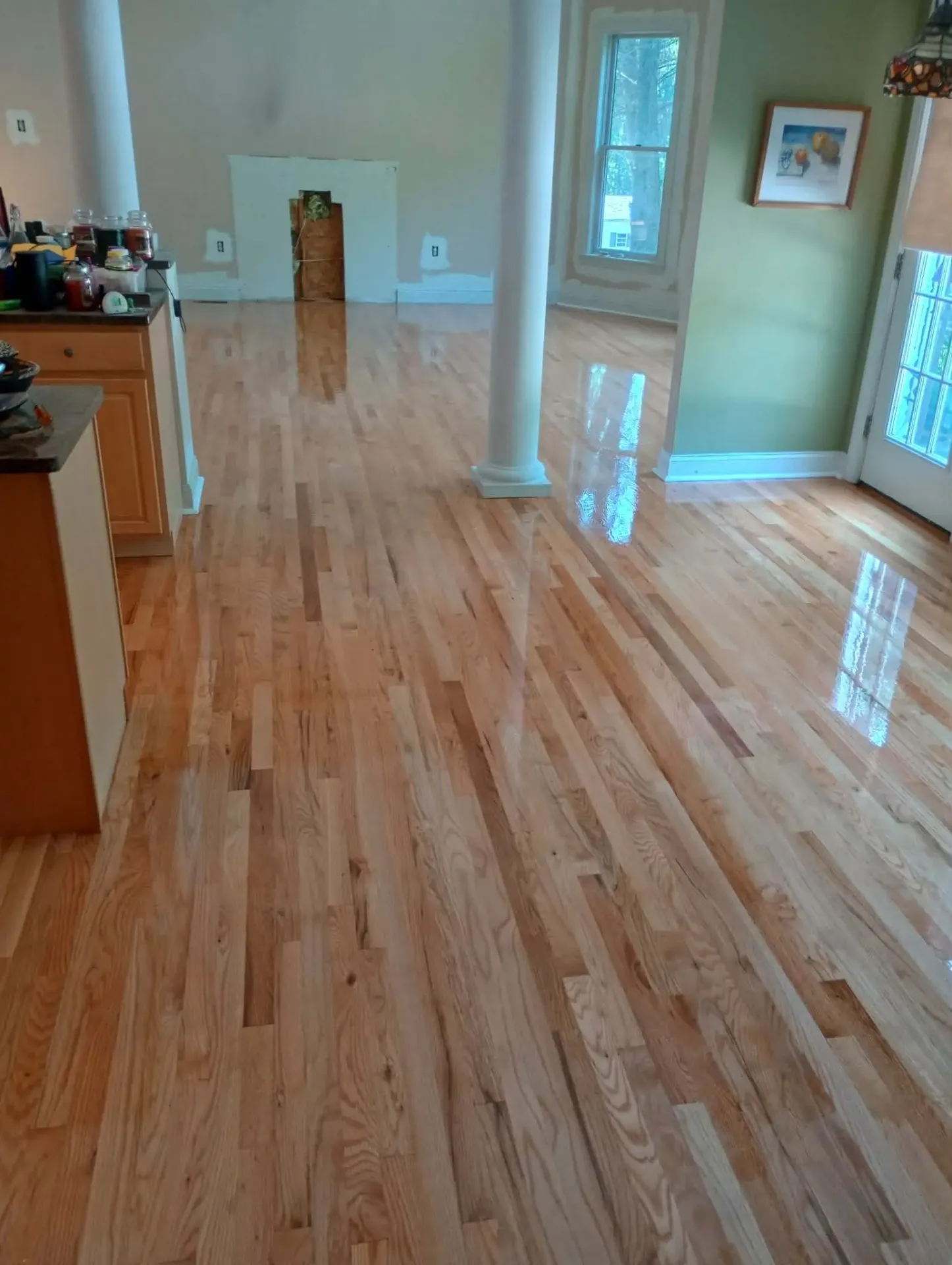 Glossy natural red oak floor freshly refinished across an open living area with white columns