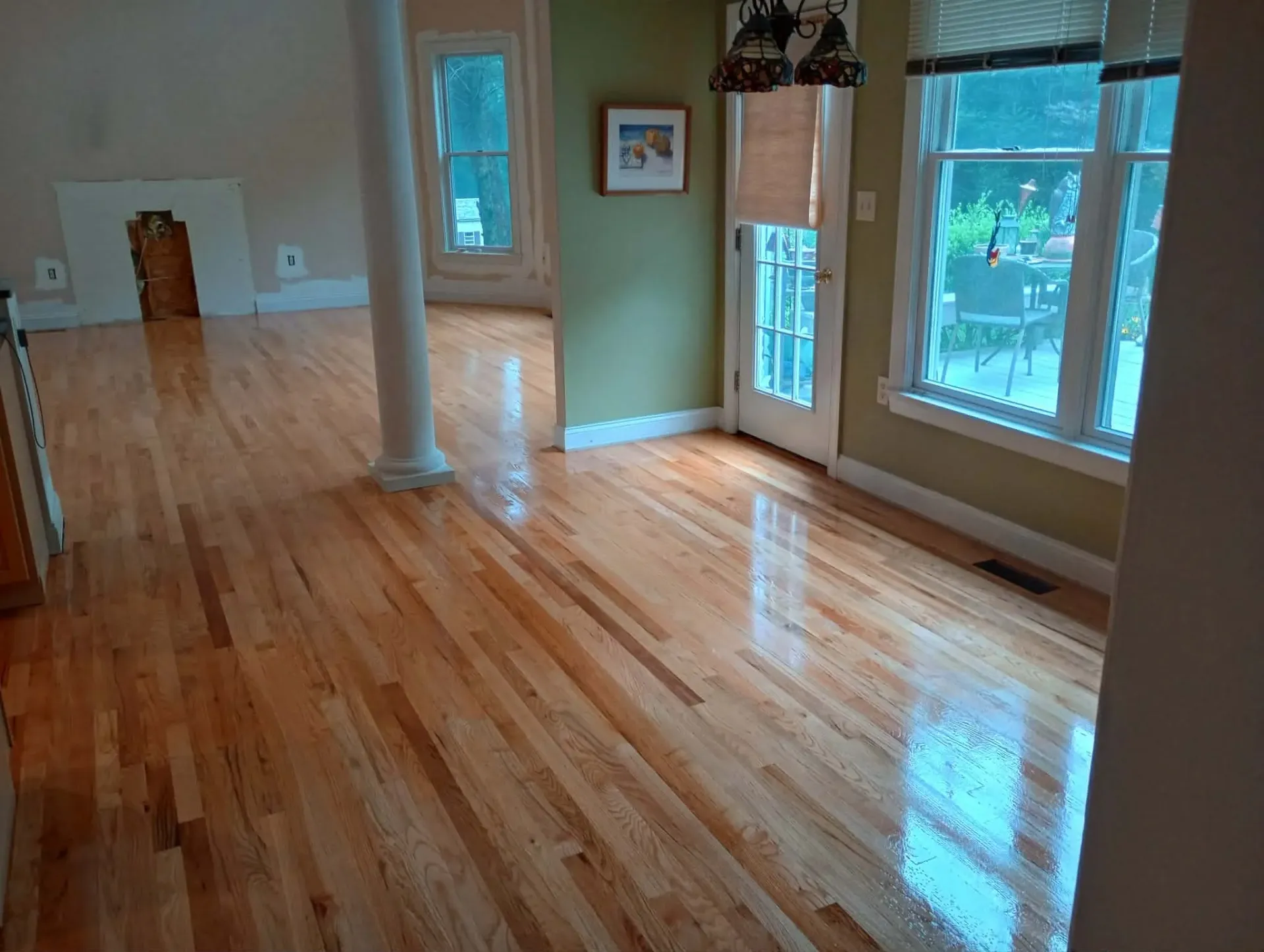 Freshly refinished glossy oak floor in a bright dining area beside a column and French door