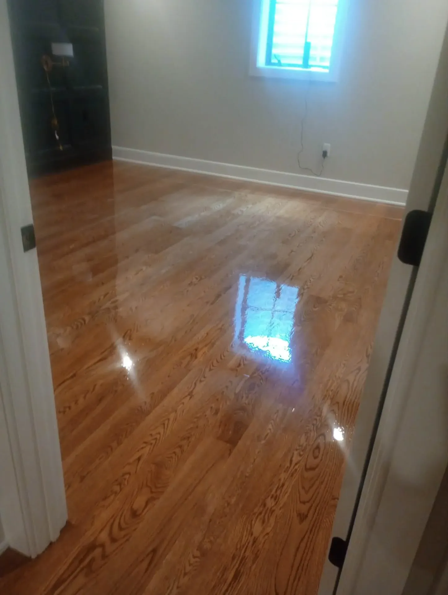 High-gloss refinished oak floor in a small room, seen through an open doorway